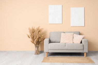 İçinde bej kanepe, kuru çiçekler ve duvarda asılı resimler olan şık bir oda.