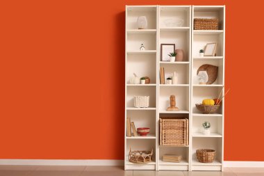 Turuncu duvarın yanında şık dekorlu raflar.