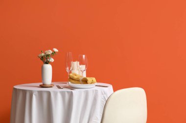 Oturma odasının iç tarafındaki turuncu duvarda çiçekler olan güzel bir masa.