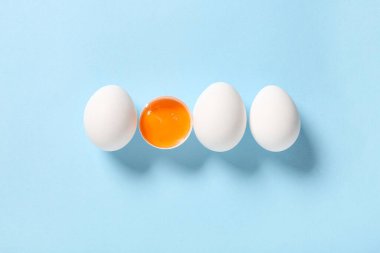 Kırılmış ve bütün tavuk yumurtaları mavi arka planda.