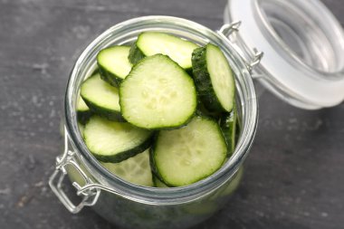 Koyu ahşap zemin üzerinde taze salatalık parçaları olan kavanoz, yakın plan.