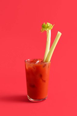 Kırmızı zemin üzerinde kereviz olan bir bardak Bloody Mary.