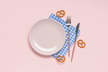 Boş tabak, çatal bıçak takımı, pembe arka planda mavi kareli peçete ve kraker.