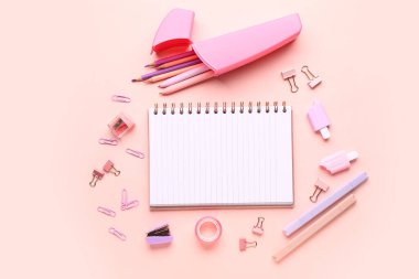 Pembe arka planda farklı kırtasiye malzemesi içeren defter.