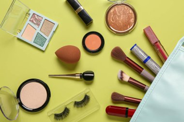 Sarı arka planda makyaj ürünleri olan şık kozmetik çanta
