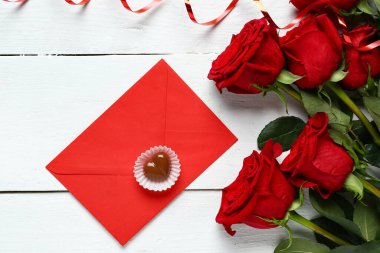 Kırmızı güller, zarf ve şeker beyaz ahşap arka planda