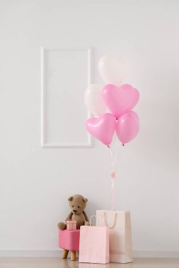 Oyuncak ayılı puf, alışveriş torbaları ve beyaz duvarın yanında kalp şeklinde balonlar. Sevgililer Günü kutlaması