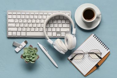 Bilgisayar klavyesi, kulaklık, defter ve kahve fincanı mavi arka planda.
