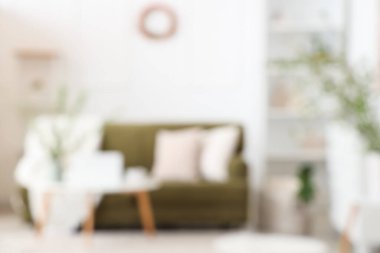 Yeşil kanepeli şık bir oda, kahve masası ve çiçek açan dallar, bulanık bir manzara.