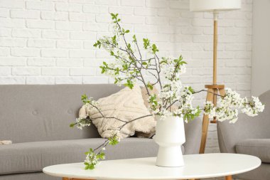 Oturma odasındaki kanepenin yanındaki sehpanın üzerinde çiçek açan bir vazo.