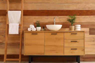 Tuvaletteki ahşap duvarın yanında lavabo ve havlular olan şık bir dolap.