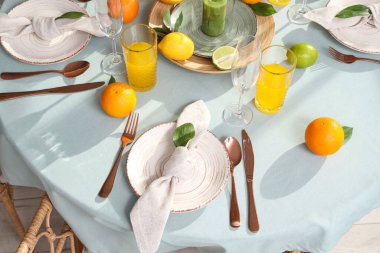 Oturma odasındaki açık mavi masa örtüsünde turunçgil meyveleri ve portakal suyu olan güzel bir masa.