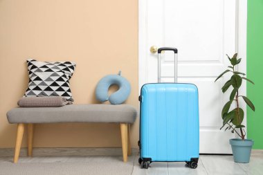 Koridordaki kapının yanındaki bankta mavi bavul ve boyun yastığı. Seyahat kavramı