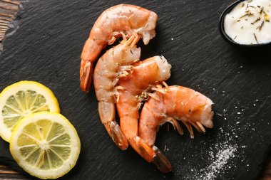 Lezzetli karidesli siyah tahta, ahşap arka planda limon ve sos, yakın plan.