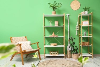 Oturma odasının içindeki yeşil duvarın yanında raflar ve ahşap koltuk.