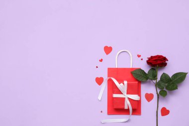 Alışveriş çantalı hediye kutusu, kağıt kalpler ve leylak arkaplanda güzel kırmızı bir gül. Sevgililer Günü kutlaması