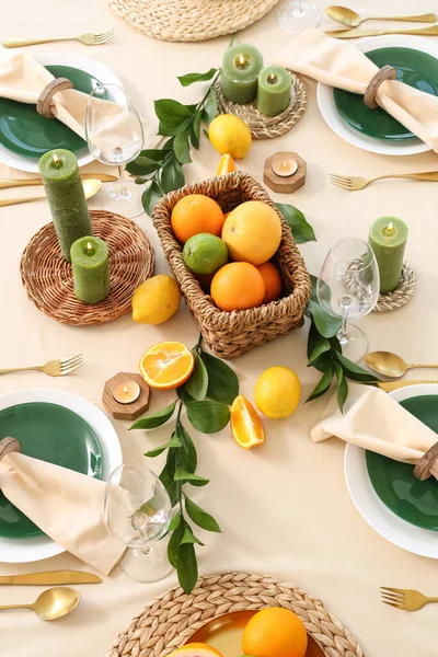 Narenciye meyveleri, yanan mumlar ve açık masa örtüsünün üzerindeki yeşil yapraklarla dolu güzel bir masa.