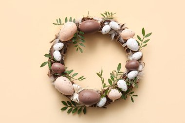 Paskalya çelengi, yeşil yapraklar ve bej arka planda yumurtalar.