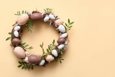 Paskalya çelengi, yeşil yapraklar ve bej arka planda yumurtalar.