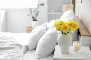 Vazo dolusu narsisli çiçek yatak odasındaki komodinin üstünde, yakın plan.