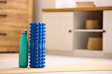 Oturma odasındaki yoga minderinde bir şişe suyla köpük silindirli.