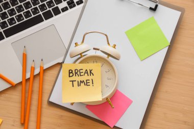 Alarm saati ve yapışkan notla yazılan kısa bir mola zamanı, masadaki dizüstü bilgisayar ve kırtasiye, üst görünüm