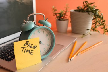 Alarm saati ve yapışkan not. Ofisteki masada mola saati ve dizüstü bilgisayar var.