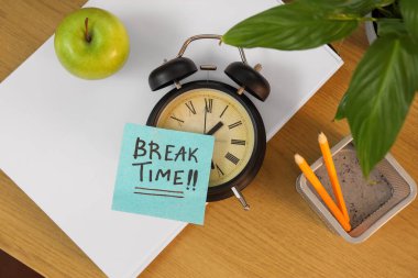 Alarm saati ve yapışkan notla yazılan BREAK Time, masadaki elma ve kırtasiye, üst görünüm