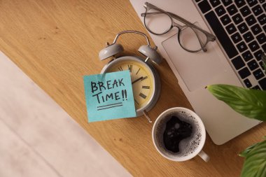 Çalar saat ve yapışkan notlar. Kısa mesaj zamanı, dizüstü bilgisayar, gözlük ve kahve kadehleri ofisteki masada, üst görünümde.