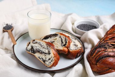 Bir parça tatlı haşhaş tohumu ve açık mavi arkaplanda bir bardak taze süt.