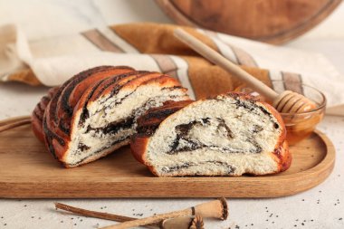 Tahta tepside kesilmiş haşhaş tohumu rulosu ve beyaz arka planda bir kase bal