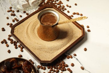 Kum ve tabakta sıcak Türk kahvesi, beyaz arka planda kurumuş hurma, yakın plan.