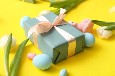 Paskalya yumurtaları, lale çiçekleri hediye kutusu ve sarı arka planda tavşan.