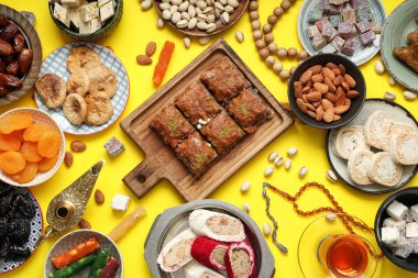 Sarı arka planda Ramazan için farklı Doğu tatlıları, tasbih ve Aladdin lambaları kompozisyonu