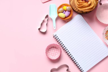 Tatlı çörek, paskalya yumurtası ve pembe arka planda pişirme aletleri olan tarifler için boş not defteri.