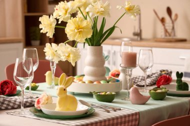 Çiçek vazosu, paskalya tavşanı, mum ve mutfakta boyanmış yumurtalarla süslü masa dekorları.