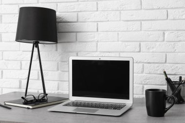 Beyaz duvarın yanında lamba ve dizüstü bilgisayarı olan modern tarz bir iş yeri.