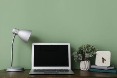 Lambalı ahşap masa, bonsai ağacı, saat ve defterler yeşil arkaplan yakınlarında.