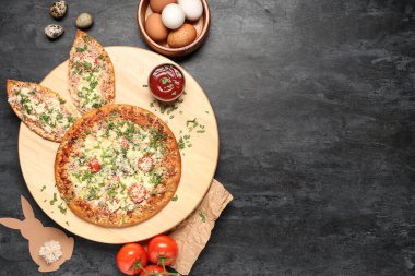 Tavşan kulaklı lezzetli pizzalar, paskalya yumurtaları, kağıt tavşanlar ve siyah grunge arka planda domatesler.