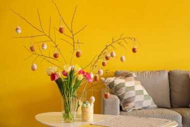 Ağaç dalları olan vazolar, oturma odasında paskalya yumurtaları ve laleler.