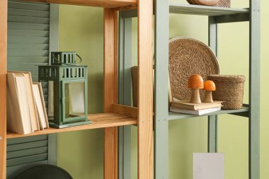 Yeşil duvarın yanında mantarlı, kitaplı ve fenerli raf ünitesi