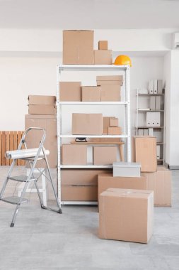 Deponun içinde raf üniteleri, karton kutular ve merdiven var.