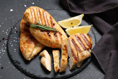 Izgara tavuk göğsü, biberiye, biber ve siyah grunge arkaplanda limon dilimleri olan tahta.