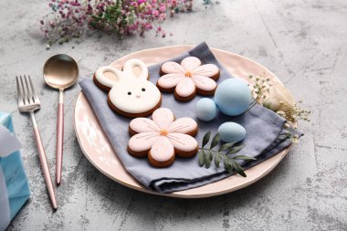 Tatlı kurabiyeler, paskalya yumurtaları ve gri arka planda çigila çiçekleri olan güzel bir masa.