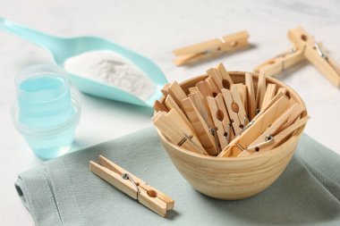 Beyaz zemin üzerinde deterjan, kumaş ve çamaşır tozu olan bir kase ahşap mandal.