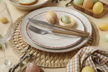 Beautiful table setting with Easter eggs and pussy willow branches on beige background, closeup