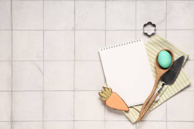 Tarifler için boş defter, Paskalya yumurtası, kurabiye ve hafif fayans üzerinde pişirme araçları içeren kompozisyon