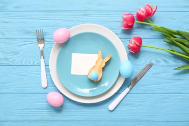 Boş kartıyla güzel bir masa, mavi ahşap arka planda Paskalya yumurtaları ve lale çiçekleri.