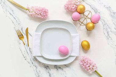 Paskalya yumurtaları ve beyaz arka planda güzel pembe çiçeklerle süslü bir masa.