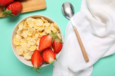 Turkuaz arka planda bir kase lezzetli mısır gevreği, çilek ve peçeteyle kompozisyon, yakın plan.